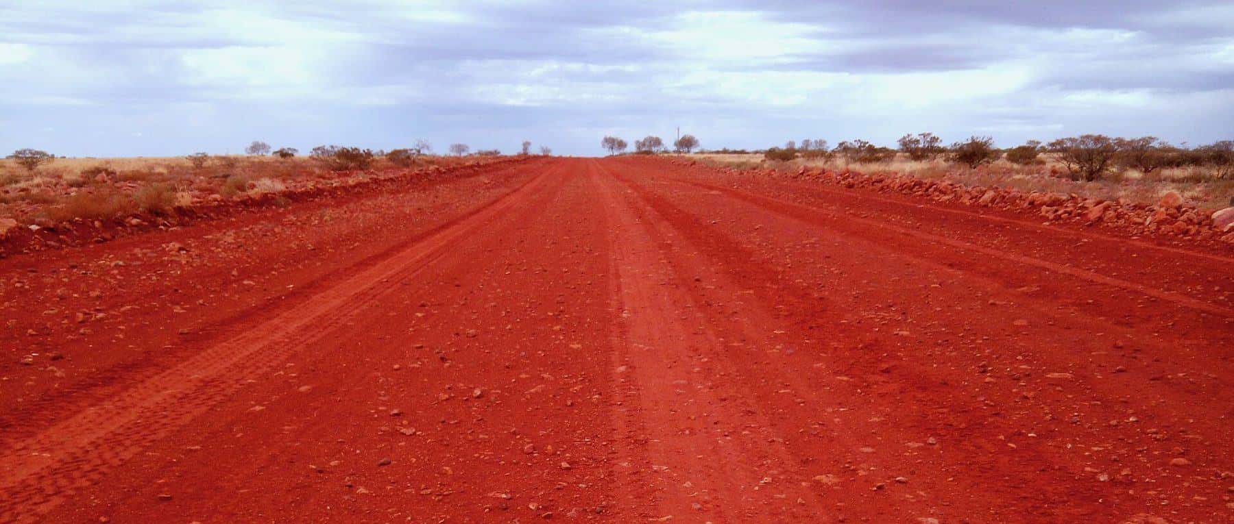 The unsealed Oodnadatta Track stretching across flat outback country